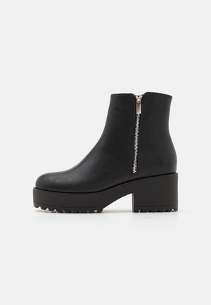 Bottes noires à la cheville avec un bout rond, en cuir synthétique texturé, fermeture éclair sur le côté, et semelle épaisse avec des rainures de traction.