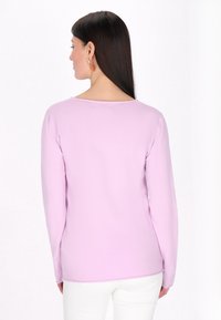 Top lung cu mânecă lungă de culoare mov deschis, cu decolteu rotund și textură netedă, siluetă ajustată și tiv cusut. Fără modele sau accente vizibile.