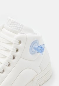 White high-top sneaker with thick sole and white laces, featuring a blue pacifier attached to the side near the ankle.