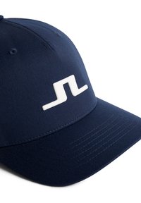 Mörkblå keps med en böjd skärm, tillverkad av mjukt tyg. Har en framträdande vit logotyp på framsidan och synliga sömmar på skärmen.