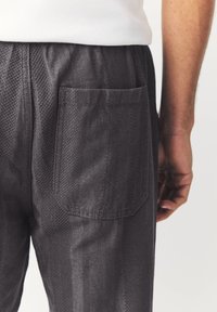 Dark gray pants with a textured fabric, featuring a rectangular back pocket. Elastic waistband visible at the top.