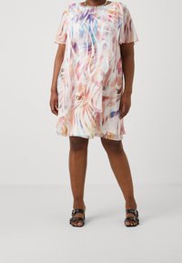 Lekka, przezroczysta sukienka o kolorowym, abstrakcyjnym wzorze w pastelowych odcieniach, z krótkimi rękawami i luźnym krojem. W zestawieniu z czarnymi sandałami.