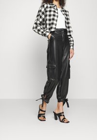 Schwarz-weißer kariertes cropped Jacke, weißes Top, schwarze Kunstleder-Cargo-Hosen mit Seitentaschen und schwarze Riemchen-Pumps.