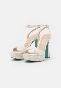 Tacchi a piattaforma bianchi con un brillante ornamento in strass, design open-toe, cinturino alla caviglia e un accento turchese sul tallone.