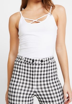 Débardeur blanc à fines bretelles avec un design croisé au niveau du décolleté, associé à un pantalon tailleur taille haute à carreaux noir et blanc.