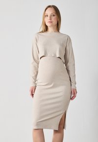 Abito a maglia beige a coste con maniche lunghe, top corto e spacco fino al ginocchio. Il tessuto ha una consistenza morbida, una silhouette aderente e una leggera elasticità.