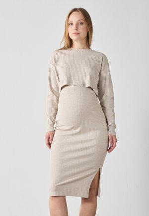 Beige geribde gebreide jurk met lange mouwen, cropped top en een hoge split tot aan de knie. De stof heeft een zachte textuur, een nauwsluitende silhouet en een subtiele rek.