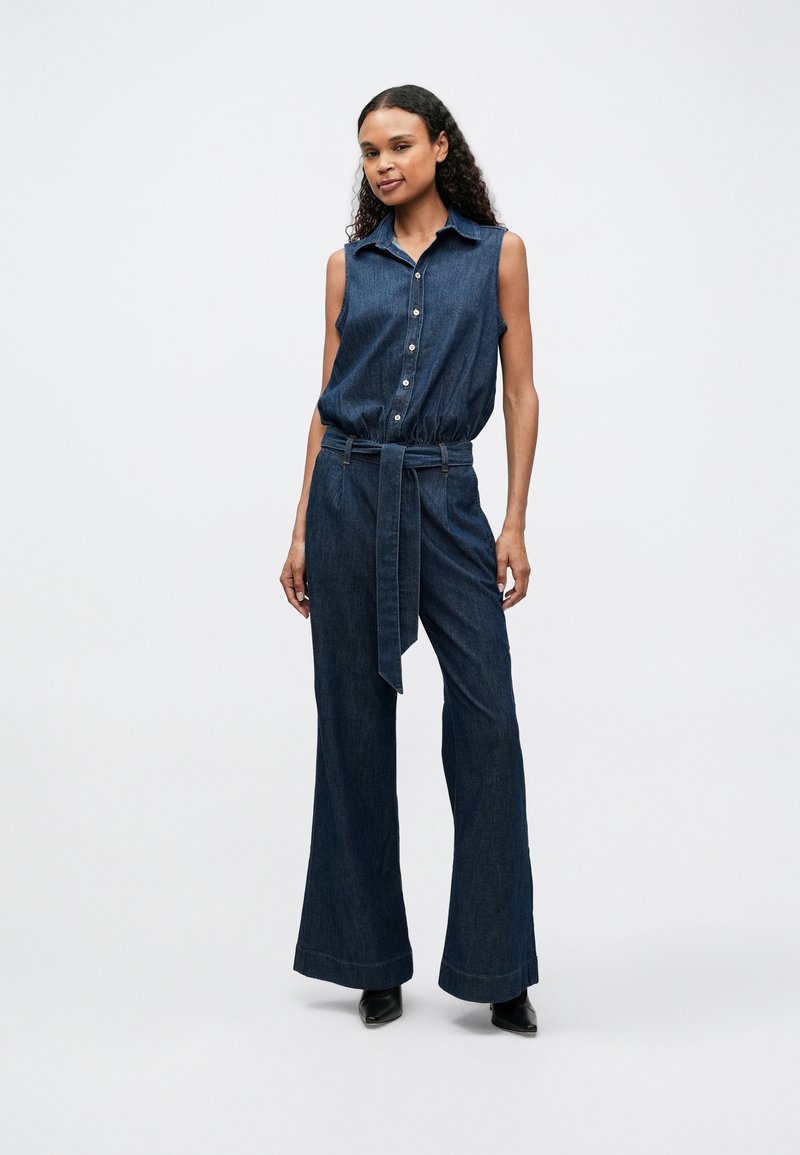 Denim jumpsuit with sleeveless design, button front, belt at the waist, and wide-leg pants. Fabric is a medium-dark blue with smooth texture.