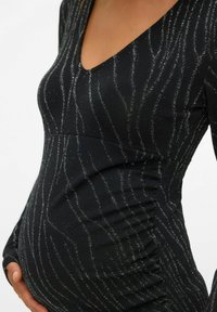 Crna haljina s prilagođenim krojem i V-izrezom, slična srebrnim okomitim prugama i nabranoj obrubi u struku, dizajnirana za trudnički siluet.