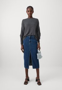 Maglione grigio a coste, gonna di jeans a vita alta con spacco frontale, sandali neri con tacco a blocco e piccola borsa azzurro chiaro.