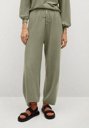 Personne portant un pantalon large en tricot vert olive avec une taille à cordon, associé à des chaussettes couleur rouille et des sandales noires à velcro.