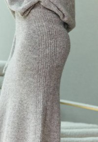 Šedé pletené šaty s jemným žebrováním, s přiléhavým střihem. Měkká tkanina se elegantně splývá a zdůrazňuje minimalistický design.