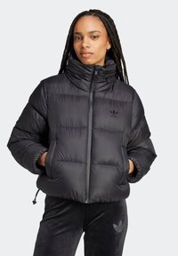 Giacca a vento nera con colletto alto, design trapuntato e chiusura con zip. Presenta il logo Adidas in nero sul petto e polsini elastici.