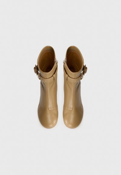 Bruna läderankelboots med en slät yta, rund tå och dekorativ spännslinga längst upp, med en sidodragkedja för stängning.