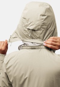 Lichtbeige waterdichte jas met capuchon, met een ritsluiting en klittenbandaccenten bij de hals, een gladde textuur en een functioneel ontwerp.