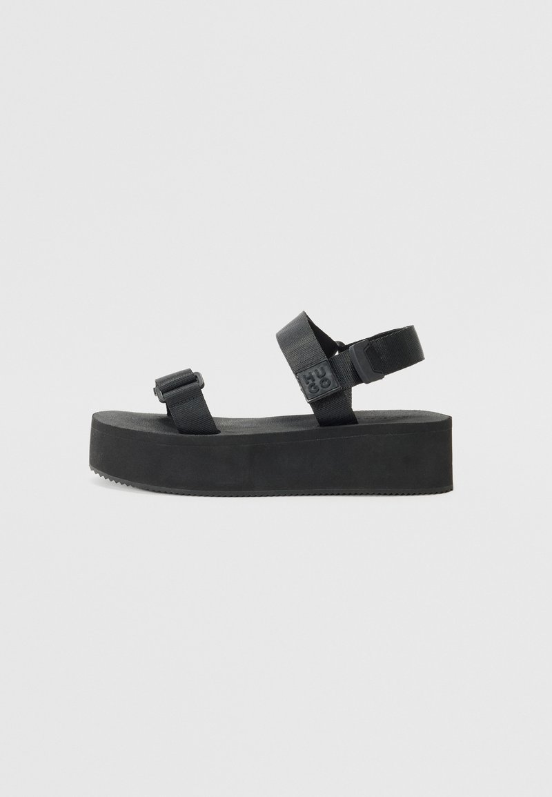 Black platform sandals with two adjustable straps made of nylon. Features a textured rubber sole and a flat base for stability.