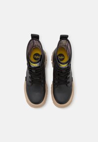 Bottes basses en cuir noir avec une finition texturée, dotées d'une semelle beige, de lacets noirs et d'un intérieur à carreaux avec une étiquette de logo visible.