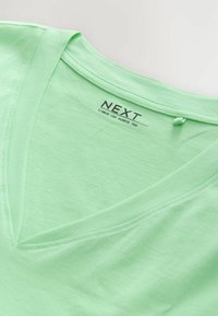 Lichtgroene v-hals t-shirt met korte mouwen, gemaakt van zachte stof, voorzien van een label met "NEXT" en bedrukte tekst op de achterkant.