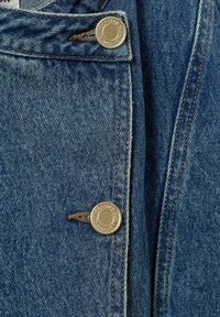 Primo piano di una giacca di jeans che mostra il tessuto blu, i bottoni metallici e i dettagli delle cuciture visibili, evidenziando la texture e la costruzione complessiva.