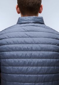 Gray puffer vest with a soft texture, featuring horizontal quilting and a standing collar. Logo visible near the neck area.