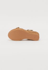 Suola in gomma marrone con grip testurizzato. Design a platform con dettagli di cucitura visibili. Presenta una tomaia in suede marrone chiaro con un accento a fibbia.