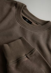 Brązowy sweter z okrągłym dekoltem i ściągaczami. Gładka tekstura z lekko zamszowym wykończeniem. Metka głosi "THE SET."