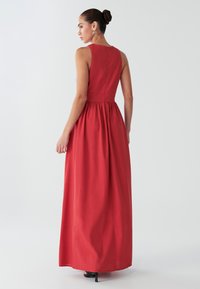 Abito lungo in tessuto rosso tinta unita; design senza maniche con corpetto aderente e gonna arricciata. Presenta una chiusura con bottoni sul retro.