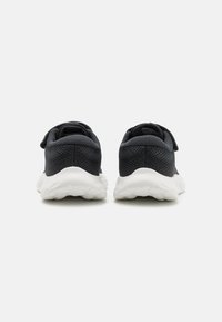 Baskets en maille noire avec une surface texturée, semelle blanche rembourrée et un design à dos fermé avec une sangle de maintien sécurisée.