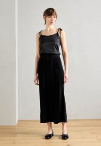 Camisole en satin noir avec des bretelles réglables à liens, associé à une longue jupe plissée en velours noir et des ballerines noires brillantes avec des nœuds.