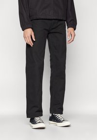 Sorte bomulds straight-leg bukser med fem lommer og et klassisk design, parret med sorte kanvas sneakers med hvide detaljer.