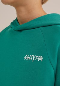 Hoodie vert en tissu lisse avec une coupe décontractée. Dispose d'une capuche et d'un logo blanc "SALTYDOG" au niveau de la poitrine.