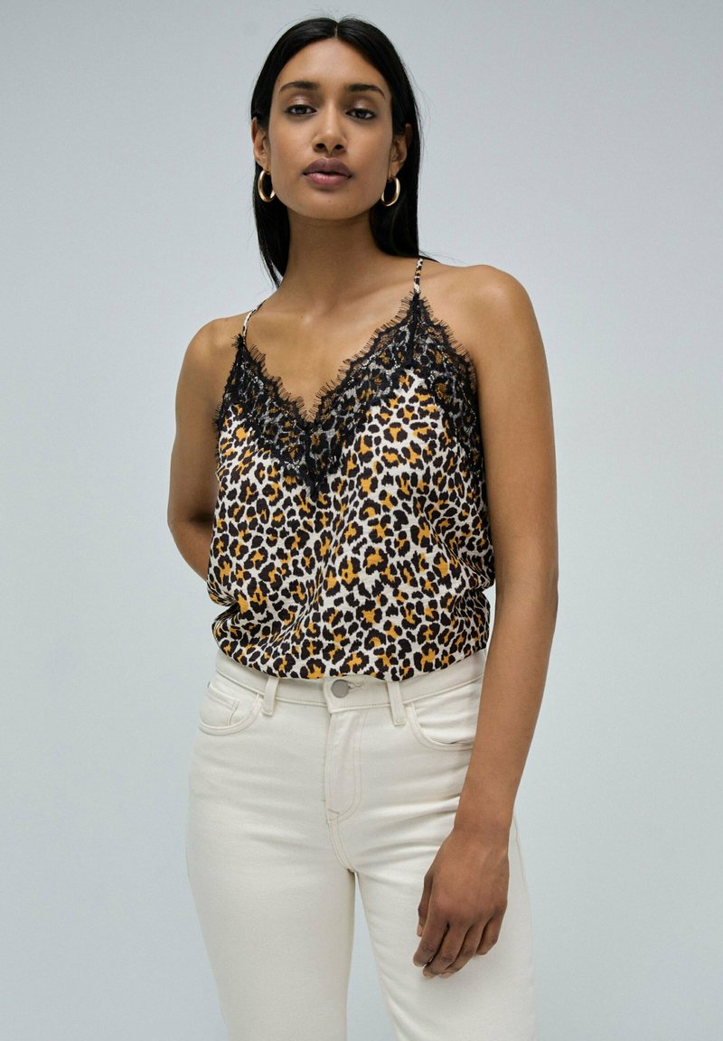 Camisole à imprimé léopard avec une bordure en dentelle noire, dotée de fines bretelles ajustables. Assortie à un jean blanc taille haute. Texture lisse.