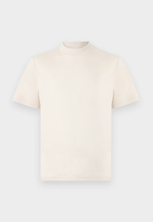 Krémové tričko s krátkým rukávem a vysokým límcem, vyrobené z měkké bavlny. Obsahuje jemně reliéfní logo na hrudi.