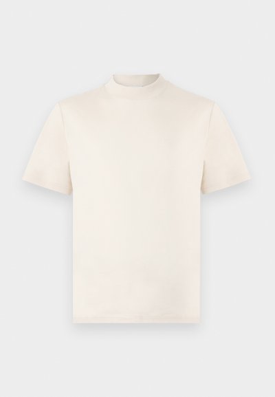 Tricou scurt cu mânecă, de culoare crem, cu un guler înalt, realizat din bumbac moale. Prezintă un logo subtil embosat pe piept.