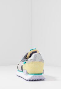 Sneaker con tomaia grigia, accenti argento e un tallone in suede giallo. Presenta una suola bianca con dettagli turchesi e suola in gomma testurizzata.