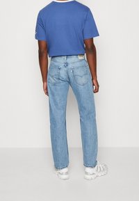 Jeans de denim azul claro con corte recto y un leve desvanecimiento, combinados con una camiseta azul de manga corta y zapatillas deportivas blancas.