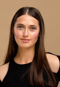 Haut noir à côtes avec des épaules dénudées, cheveux longs et raides de couleur foncée, et maquillage naturel. L'arrière-plan est d'une couleur beige chaud.