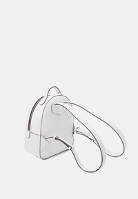White backpack made of textured material, featuring a smooth zipper, brown accents, rounded shape, and two adjustable straps.