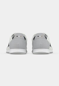 Para białych i szarych sportowych trampek widzianych od tyłu, prezentujących teksturowane, szare ochrony pięty oraz białe podeszwy na białym tle.