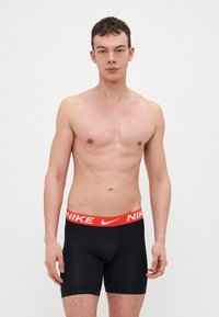 Fekete boxeralsó széles piros derékrésszel, amelyen fehér "NIKE" felirat található. Rugalmas anyagból készült, testhezálló fazonnal.