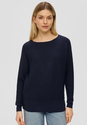 Pull en maille côtelée bleu marine avec un col bateau, des manches longues et une coupe décontractée, accompagné d'un jean bleu clair. Tissu texturé.