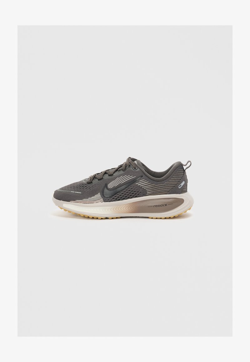 Buty sportowe z ciemnoszarej siateczki z czarnymi akcentami, z beżową, amortyzującą podeszwą oraz smukłą, lekką konstrukcją. Wyraźne logo po boku.