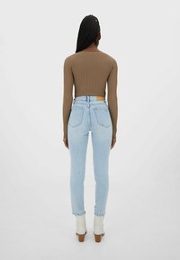 En åtsittande brun långärmad topp kombinerad med högmidjade ljusblå skinny jeans. Påfallande detaljer inkluderar en framträdande midjeband och söms accent.