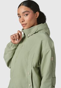 Light green, hooded jacket with elastic cuffs, zip closure, snap buttons, and a logo patch on the sleeve. Smooth, lightweight fabric.