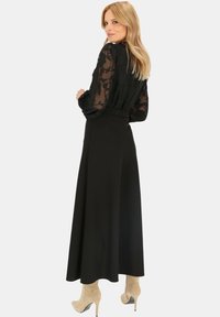 Czarna przezroczysta bluzka w kwiatowy wzór z długimi rękawami, zestawiona z czarną spódnicą o wysokim stanie i beżowymi botkami za kostkę.