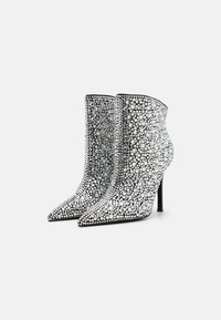 Bottines à talons aiguilles recouvertes de strass argentés et transparents, avec un bout pointu et un fin talon haut. Doublure intérieure noir lisse.