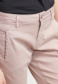 Ljusrosa byxor i bomull med dragkedja, platt framsida och sidofickor. Tyget har en slät struktur med minimala sömdetaljer.