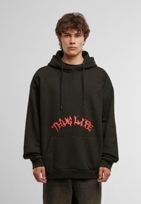 Sudadera negra con bolsillo frontal, capucha con cordón y un audaz texto gráfico en rojo "THUG LIFE" en la parte delantera en una fuente estilizada.
