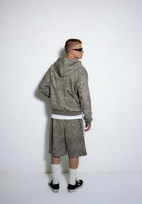 Szary zestaw z kapturem i szortami w wzór paisley, wykonany z miękkiego materiału. Model nosi czarne sneakersy i białe skarpetki, widziany z tyłu.