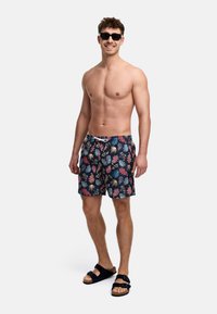 Badedrakt med tropisk bladmønster i sterke farger, laget av lett stoff. Designet med elastisk midje og snor.